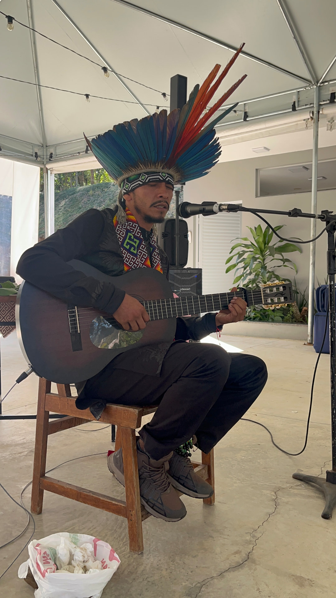 Ixã Txaná cantando com cocar e violão